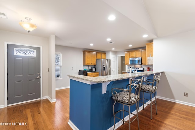 kitchen featuring stainless steel appliances, a breakfast bar area, hardwood / wood-style floors, and kitchen peninsula