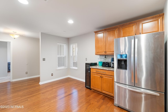 kitchen with decorative backsplash, light stone countertops, light hardwood / wood-style floors, and stainless steel refrigerator with ice dispenser