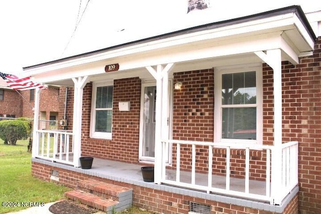 entrance to property featuring a porch and brick siding