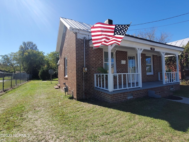 view of front of property featuring a porch, brick siding, fence, and a front lawn