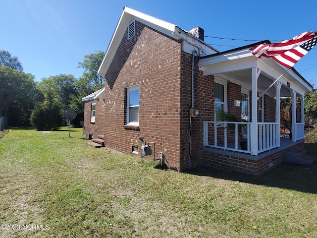 view of property exterior featuring covered porch, a chimney, a lawn, and brick siding