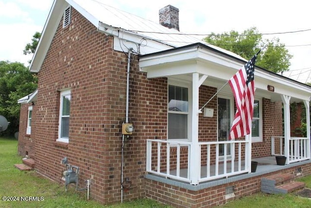 view of side of home with a porch, a chimney, and brick siding