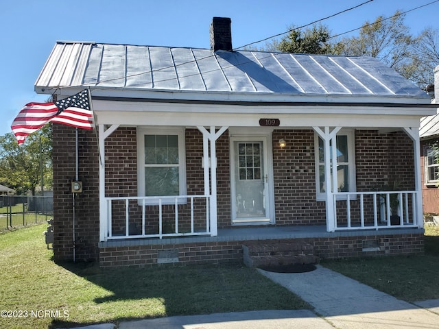 view of exterior entry featuring metal roof, covered porch, brick siding, a standing seam roof, and a chimney