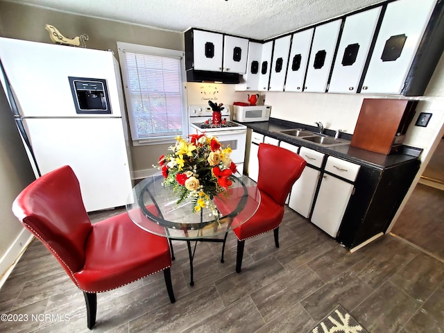 kitchen featuring dark countertops, a sink, a textured ceiling, white appliances, and under cabinet range hood