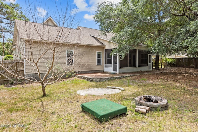 back of house with a lawn, a sunroom, and an outdoor fire pit