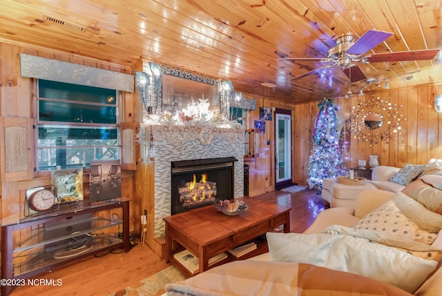 living room with a stone fireplace, wood finished floors, wood ceiling, and wood walls