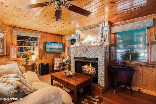 living area with wood finished floors, wooden walls, a stone fireplace, wooden ceiling, and ceiling fan