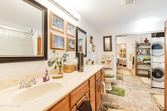 full bathroom featuring a sink, stone finish flooring, ensuite bath, stacked washing maching and dryer, and double vanity