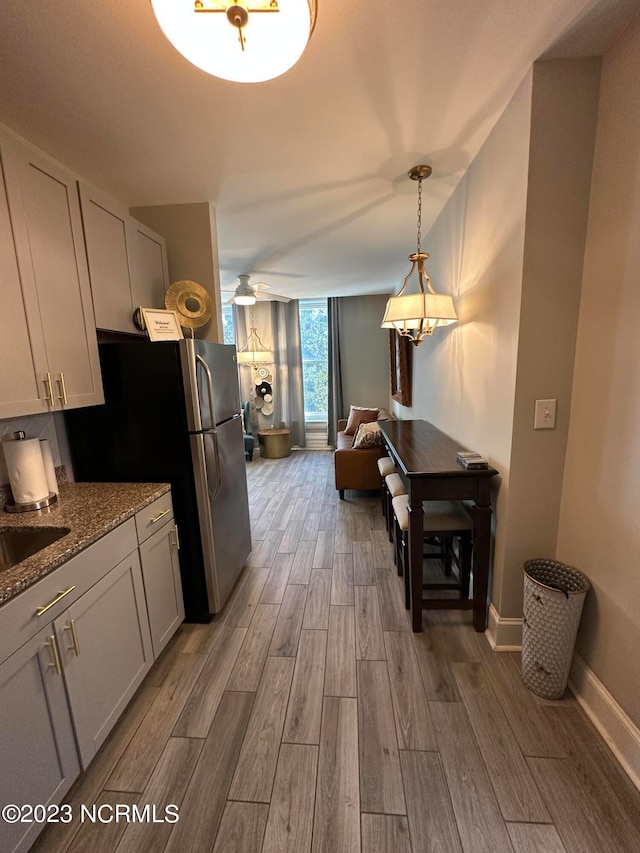 kitchen with hanging light fixtures, stainless steel fridge, light stone counters, white cabinets, and hardwood / wood-style flooring