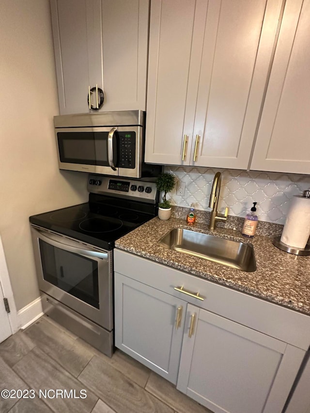 kitchen with appliances with stainless steel finishes, sink, dark stone counters, and decorative backsplash