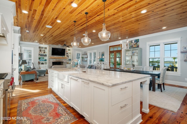 kitchen with a large island with sink, wood-type flooring, sink, built in features, and white cabinetry