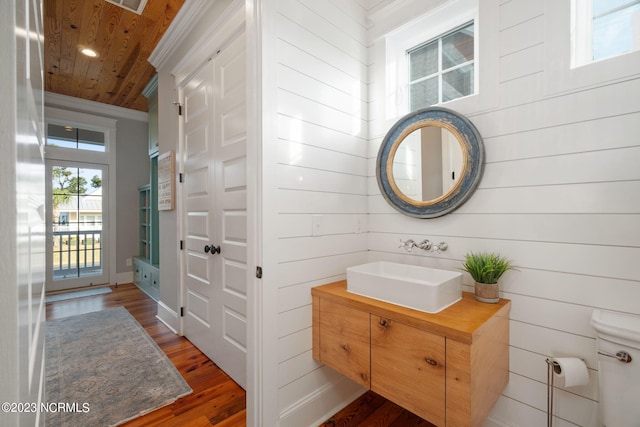 bathroom with wood-type flooring, toilet, wooden ceiling, wooden walls, and vanity