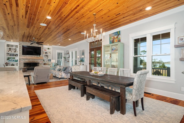 dining room with wood ceiling, hardwood / wood-style floors, built in shelves, ceiling fan with notable chandelier, and a fireplace