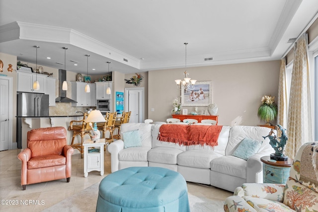 living room with light tile floors, an inviting chandelier, ornamental molding, and a tray ceiling