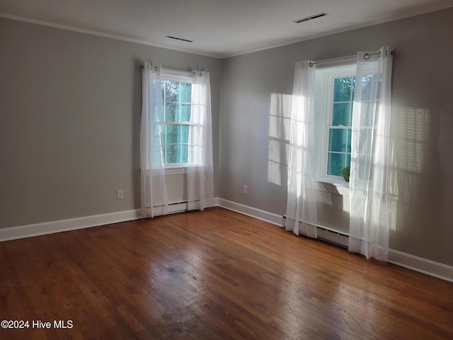 empty room featuring ornamental molding, plenty of natural light, wood-type flooring, and a baseboard heating unit