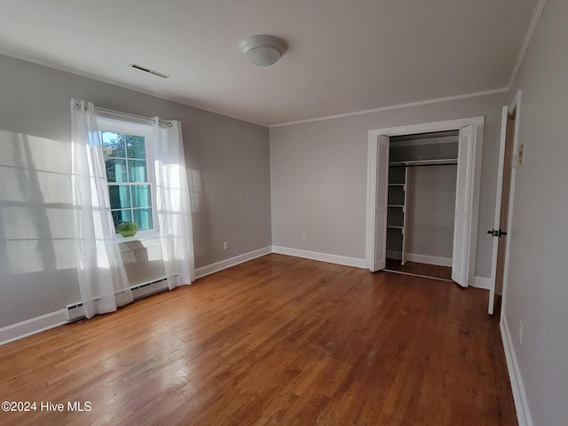 unfurnished bedroom featuring wood-type flooring, baseboard heating, a closet, and crown molding