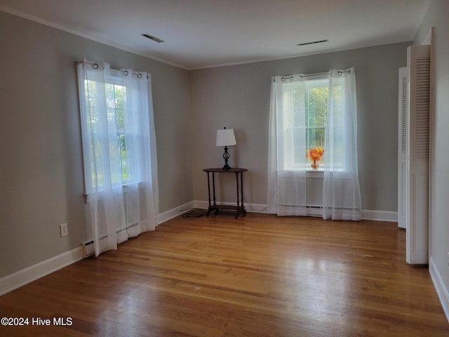 unfurnished room with baseboard heating, plenty of natural light, ornamental molding, and hardwood / wood-style flooring