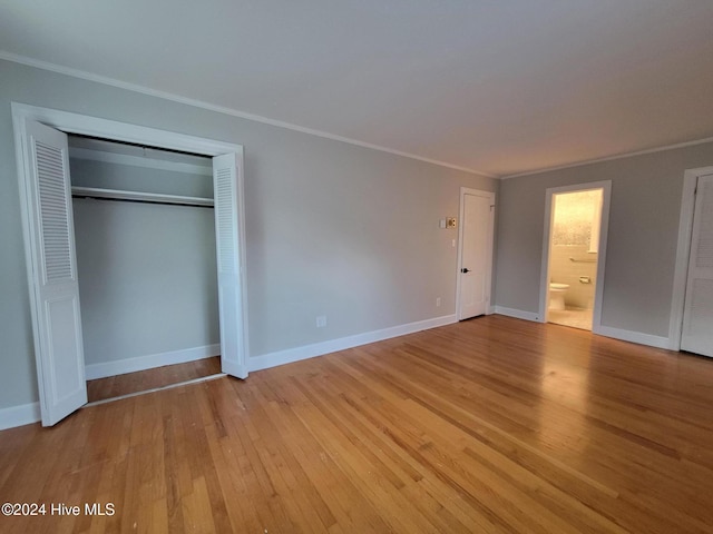 unfurnished bedroom featuring ensuite bathroom, a closet, light wood-type flooring, and ornamental molding