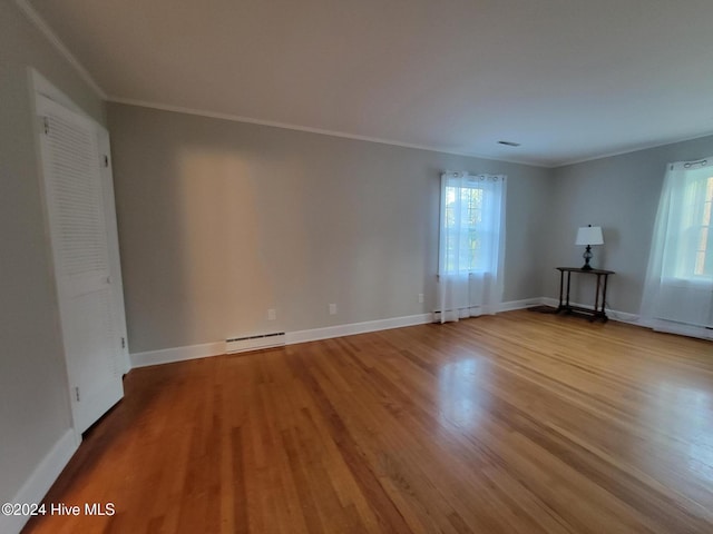 empty room featuring hardwood / wood-style floors, baseboard heating, and crown molding