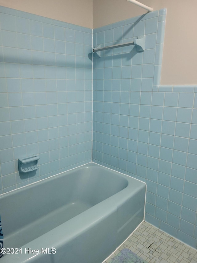 bathroom with tiled shower / bath combo, tile patterned floors, and tile walls