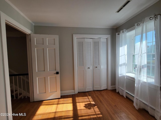 unfurnished bedroom featuring hardwood / wood-style floors, a baseboard radiator, a closet, and crown molding