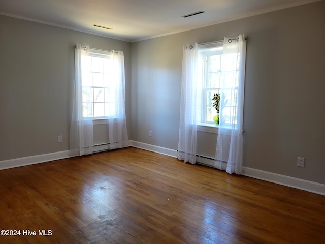 empty room with hardwood / wood-style flooring, a healthy amount of sunlight, ornamental molding, and a baseboard radiator