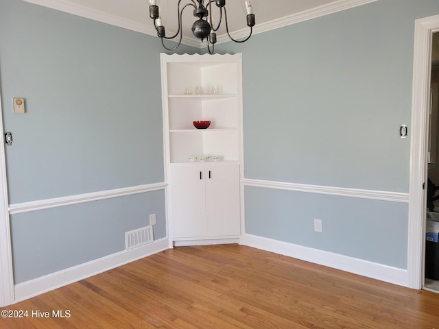 empty room with wood-type flooring, built in features, ornamental molding, and a chandelier