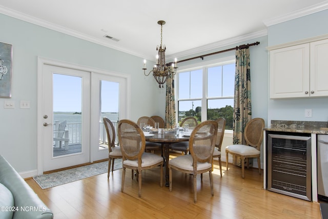 dining area featuring wine cooler, a water view, ornamental molding, and light hardwood / wood-style flooring