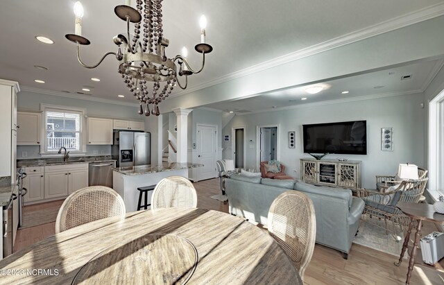 dining room featuring crown molding, sink, light hardwood / wood-style flooring, and ornate columns