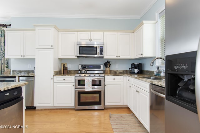 kitchen with appliances with stainless steel finishes, sink, dark stone counters, light hardwood / wood-style floors, and crown molding