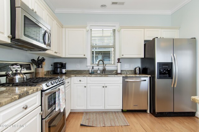 kitchen with stainless steel appliances, sink, light wood-type flooring, dark stone countertops, and ornamental molding