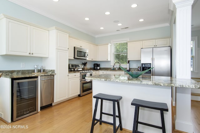 kitchen with crown molding, appliances with stainless steel finishes, dark stone countertops, and beverage cooler