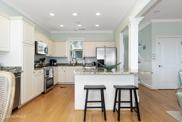 kitchen with a kitchen island, stainless steel appliances, light hardwood / wood-style floors, ornate columns, and stone countertops