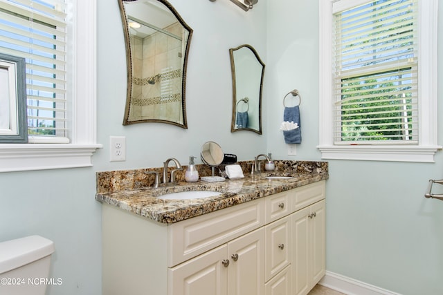 bathroom with double vanity, toilet, and plenty of natural light