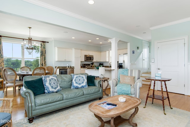 living room featuring ornamental molding, ornate columns, a chandelier, and light hardwood / wood-style floors