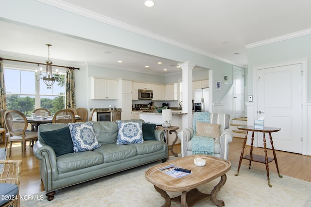 living room with ornamental molding, a chandelier, decorative columns, and light hardwood / wood-style flooring