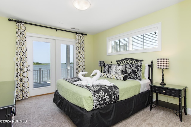 bedroom with a water view, light carpet, and access to outside