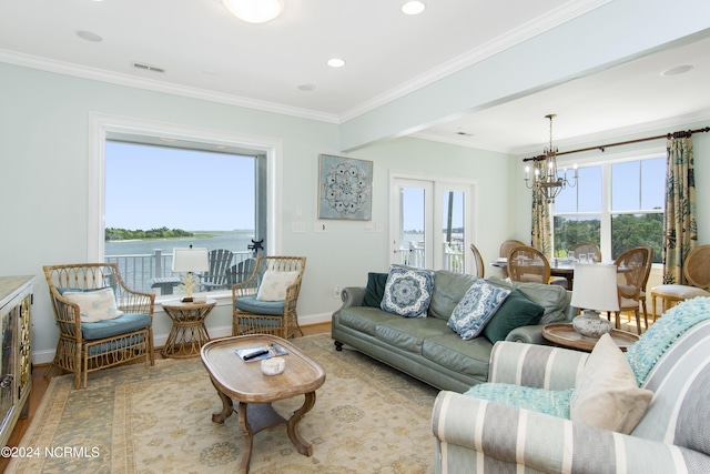 living room with ornamental molding, an inviting chandelier, a water view, and light hardwood / wood-style floors