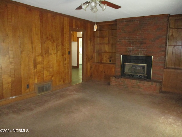 unfurnished living room featuring carpet flooring, wood walls, ceiling fan, and a brick fireplace