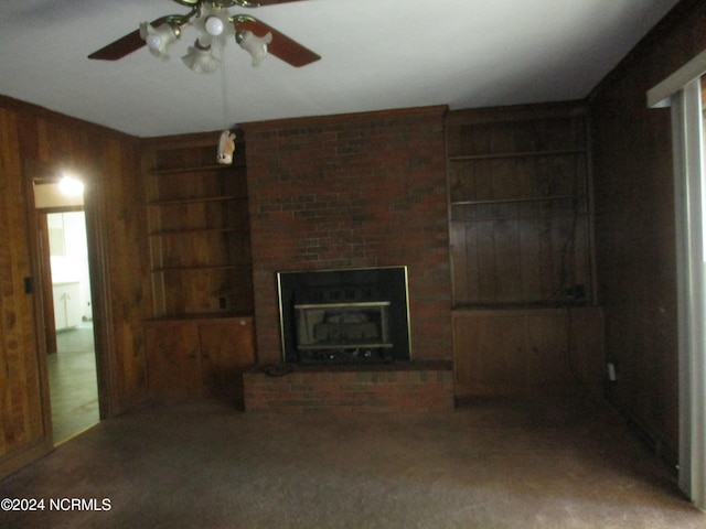 unfurnished living room with carpet flooring, ceiling fan, built in features, a fireplace, and wood walls