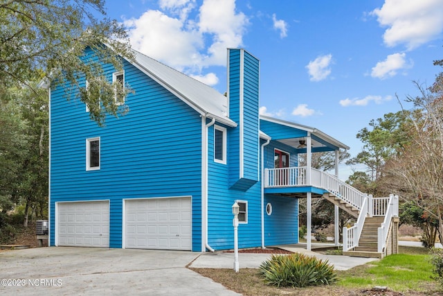 exterior space featuring a chimney, concrete driveway, an attached garage, a ceiling fan, and stairs