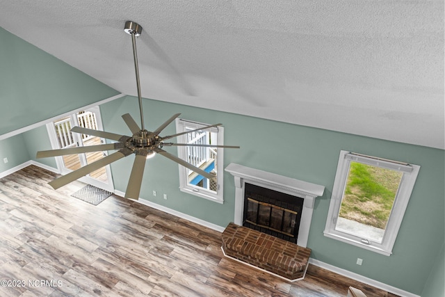 unfurnished living room featuring hardwood / wood-style floors, high vaulted ceiling, a brick fireplace, ceiling fan, and a textured ceiling