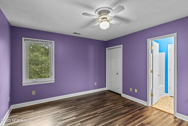 unfurnished bedroom with ensuite bath, ceiling fan, dark wood-type flooring, and a textured ceiling