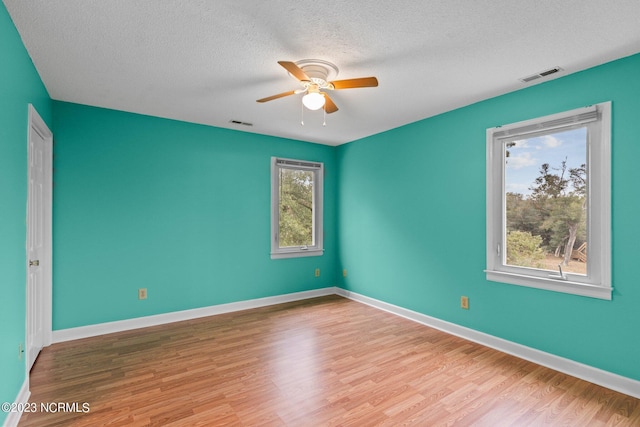 spare room featuring ceiling fan, a healthy amount of sunlight, a textured ceiling, and light hardwood / wood-style flooring