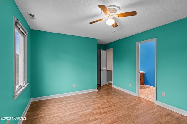 unfurnished bedroom with ceiling fan, ensuite bathroom, light wood-type flooring, and a textured ceiling