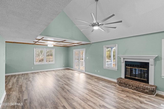 unfurnished living room featuring ceiling fan, light hardwood / wood-style floors, lofted ceiling, a textured ceiling, and a fireplace