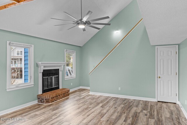 unfurnished living room featuring light hardwood / wood-style floors, a healthy amount of sunlight, lofted ceiling, and a brick fireplace