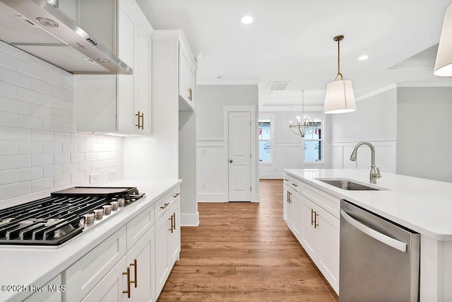 kitchen featuring pendant lighting, white cabinetry, sink, stainless steel appliances, and wall chimney range hood