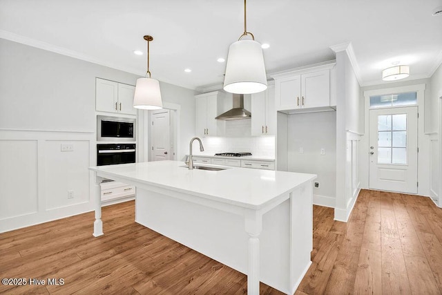 kitchen with black oven, sink, white cabinets, ornamental molding, and a kitchen island with sink