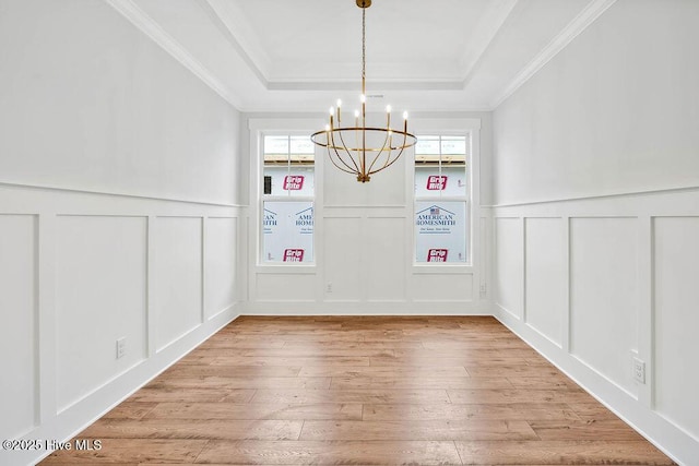 unfurnished dining area with a chandelier, ornamental molding, wood-type flooring, and a raised ceiling